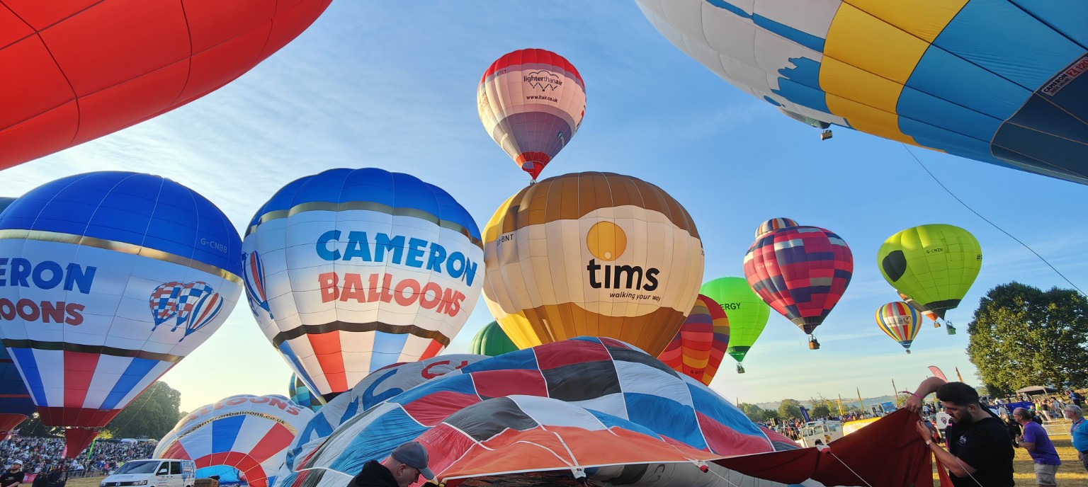 Hot air balloons at different stages of inflation on a balloon fiesta launch field under blue skies